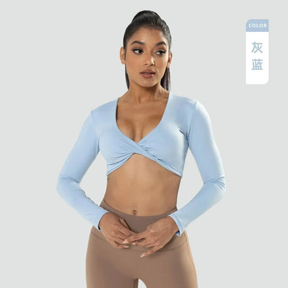 A light blue long-sleeved crop top features a V-neckline with a twisted front detail worn by a woman with a high ponytail against a solid light grey background.