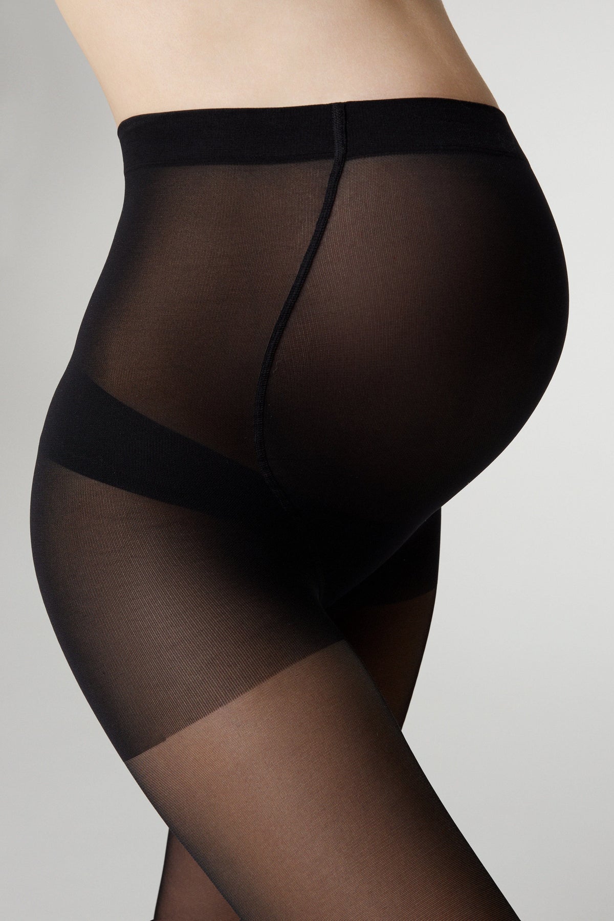 Black maternity tights worn by a pregnant person against a plain light gray background.