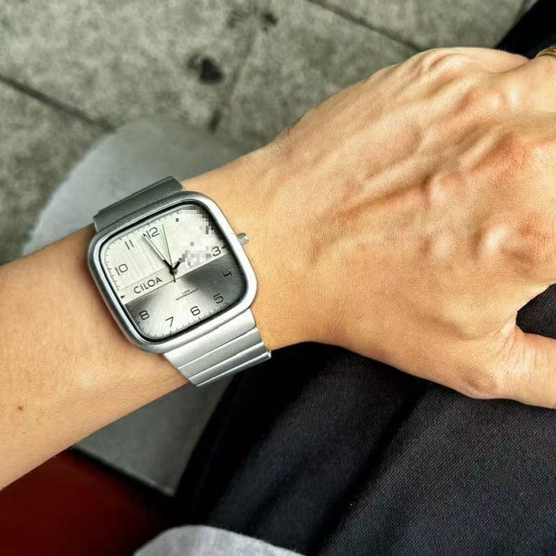 A silver-toned square wrist watch with a light-colored face featuring black numerals and a metallic link bracelet, worn on a person's wrist.