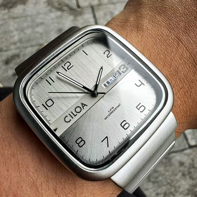 A square-faced wristwatch with a silver metallic dial featuring black numerals, a date display window, and a silver-toned metal link band worn on a person's wrist.