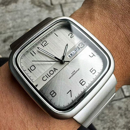 A square-faced wristwatch with a silver metallic dial featuring black numerals, a date display window, and a silver-toned metal link band worn on a person's wrist.