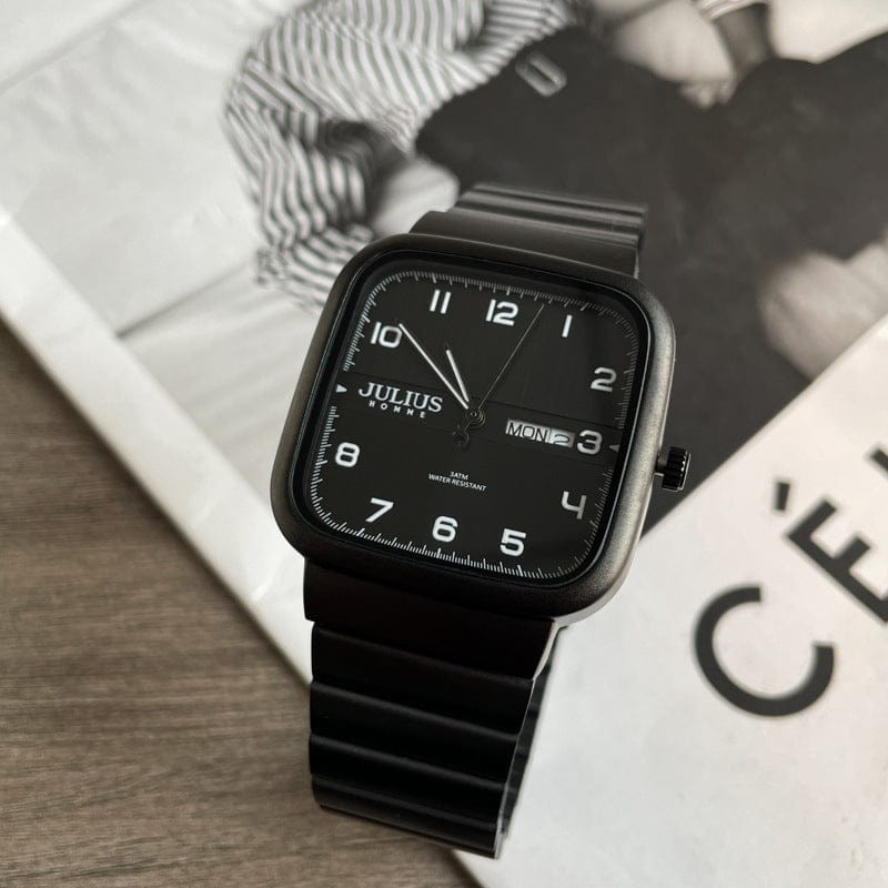 A black square-faced analog watch with a matching black linked strap sits on top of a black and white fashion magazine.