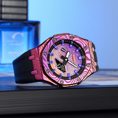 A wrist watch with a black rubber strap and an octagonal metallic bezel featuring a vibrant pink and purple patterned design rests on a dark surface in front of a blue glass bottle.
