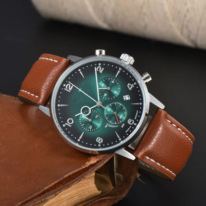 A round watch with a green sunburst dial featuring three sub-dials, a date window, and silver indices on a brown leather strap resting against a brown leather notebook.