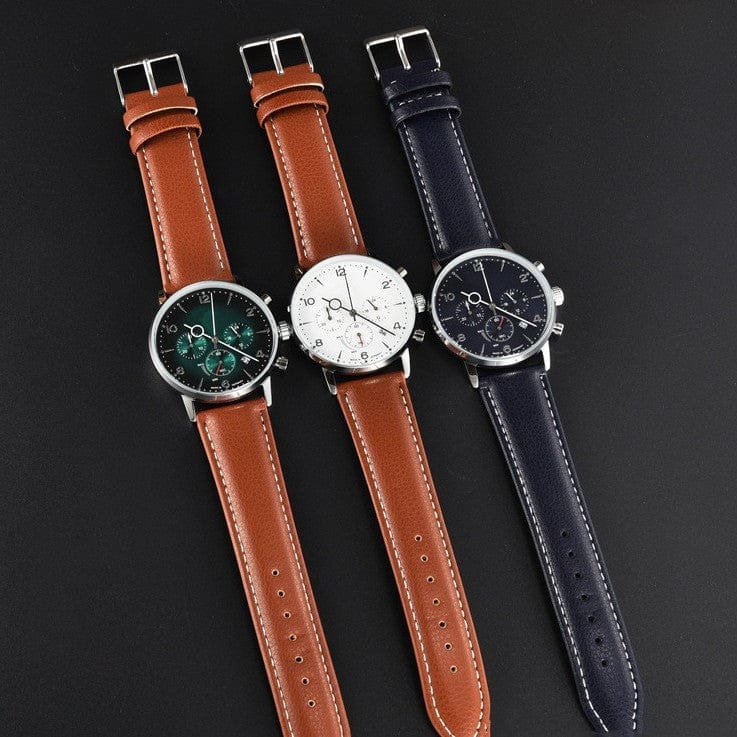 Three wristwatches with round silver cases and leather straps are arranged side-by-side on a dark background, featuring a green dial with a tan strap, a white dial with a tan strap, and a navy blue dial with a matching navy blue strap.