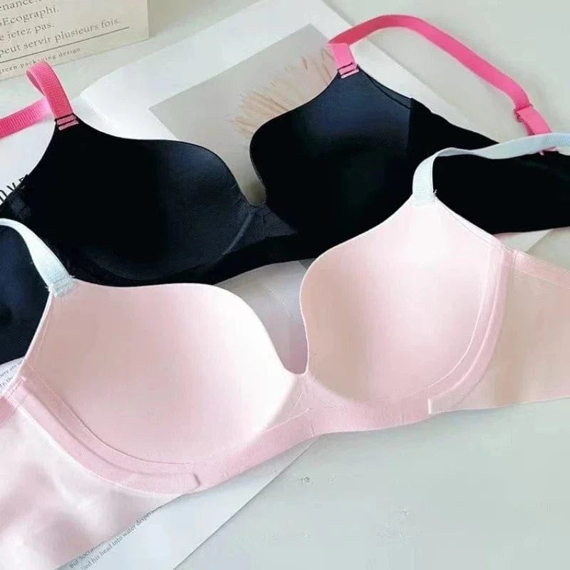 Two seamless bras, one black with bright pink straps and one light pink with white straps, lie on a white surface next to a piece of paper.