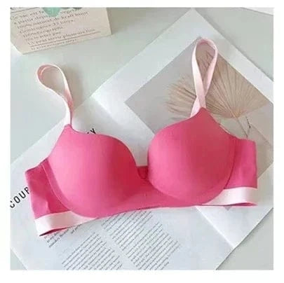 A hot pink seamless wireless bra with pale pink adjustable straps and a matching bottom band, laid flat on a white paper surface.