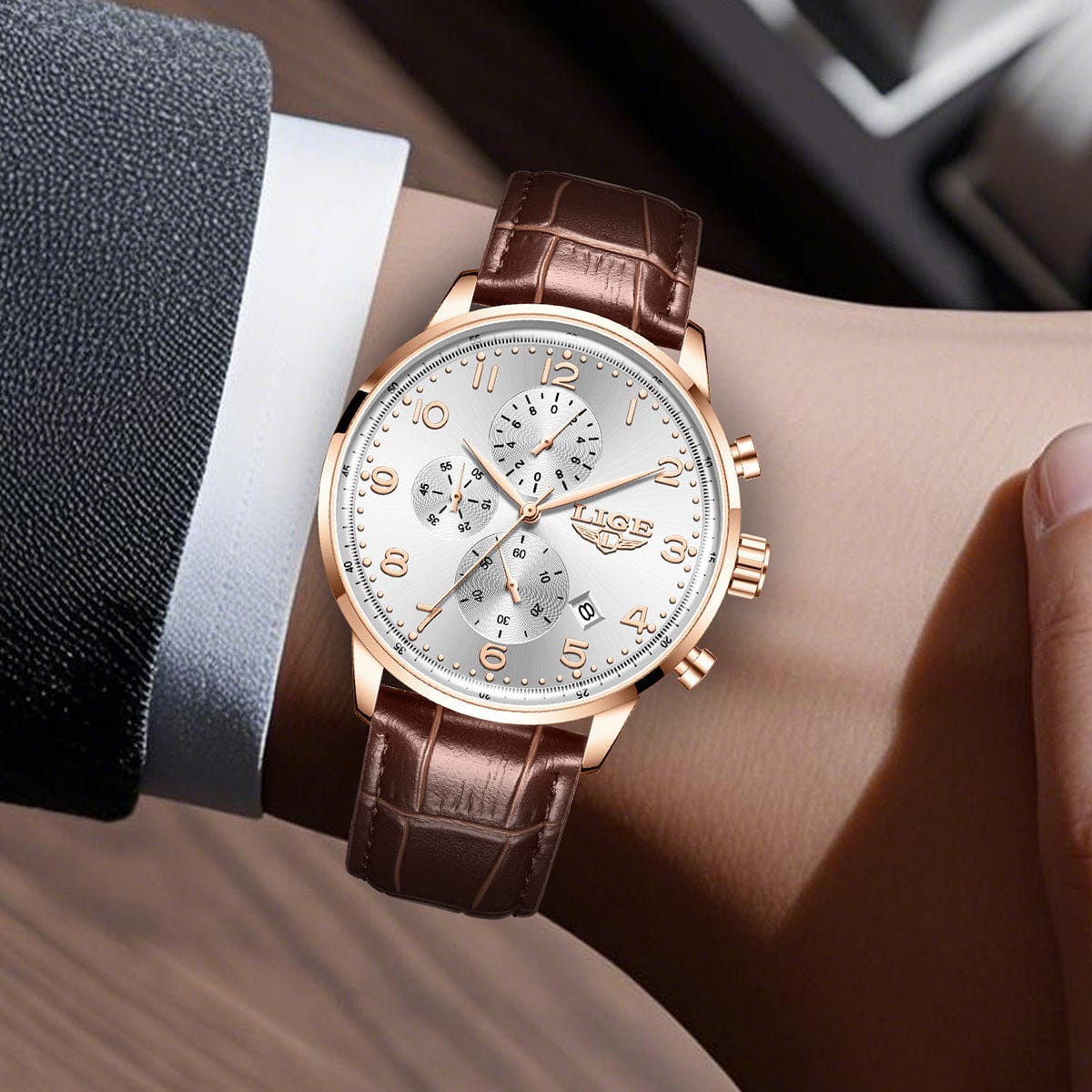 A wrist watch with a white dial, rose gold indices and hands, and three sub-dials, featuring a brown leather strap worn on a wrist.