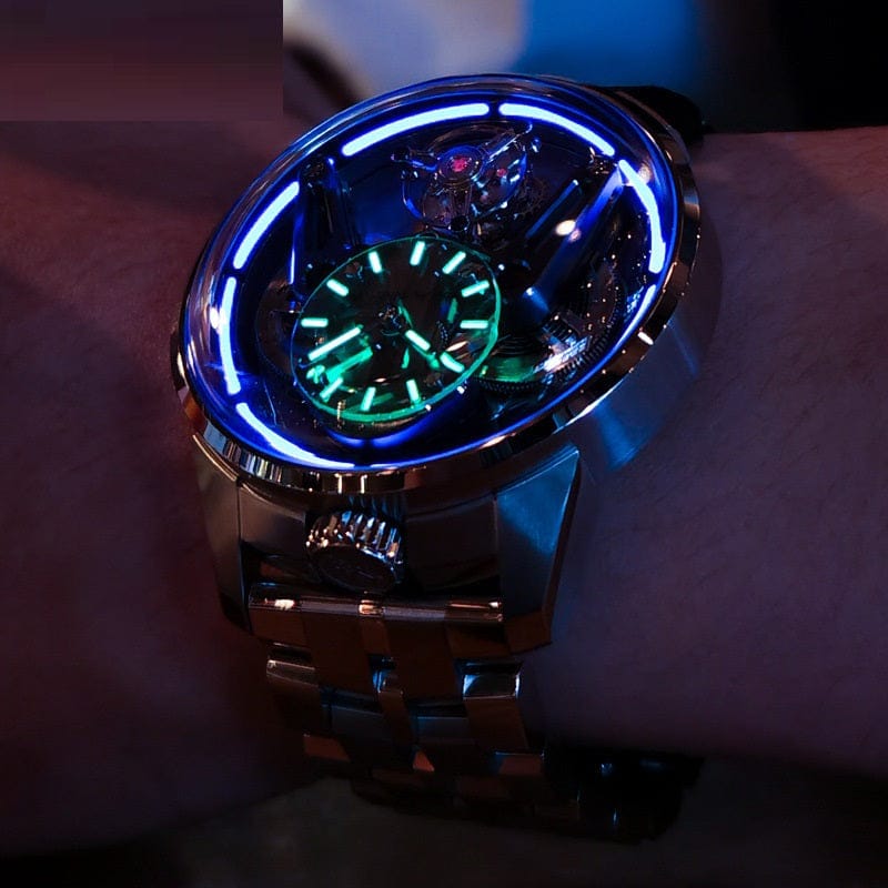 A round metallic wristwatch with a glowing blue light ring around the dial and bright green luminescent clock hands and indices on the arm.