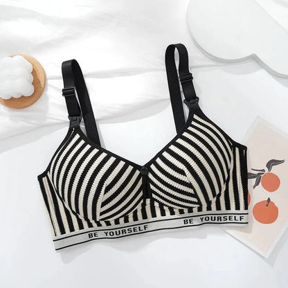 A black and white striped nursing bra with adjustable straps sits on a white surface next to a decorative white candle and a small print featuring oranges.