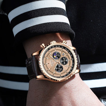 A gold-toned chronograph wristwatch with a light gold dial, three sub-dials, a moon phase display, and a dark brown leather strap worn on a wrist.