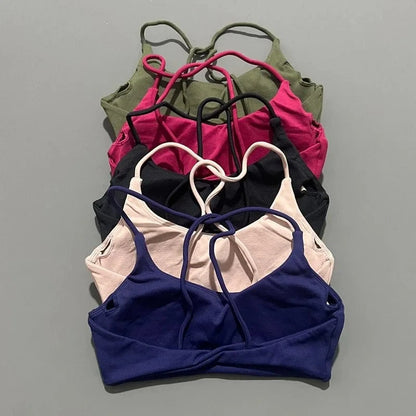Five sports bras stacked vertically on a gray background, featuring a twist-front hem and thin crisscross straps in olive green, magenta, black, light pink, and navy blue.