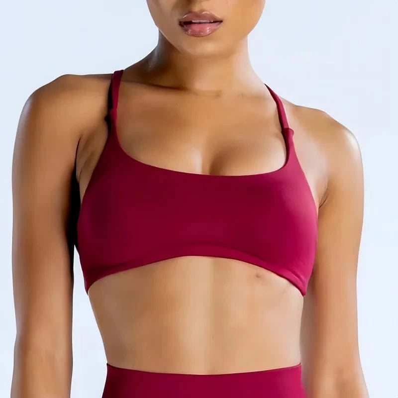 A dark red cropped sports bra with thin spaghetti straps and a scoop neckline worn by a person.