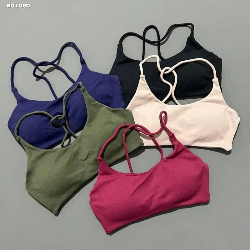 Five sports bras with thin crisscross straps displayed on a gray background in black, white, olive green, deep purple, and magenta.