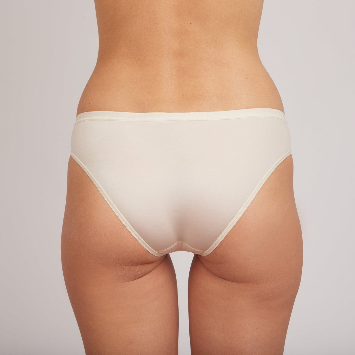 A pair of beige bikini-style underwear viewed from the back on a person against a neutral background.