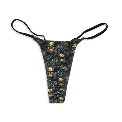 A thong with a black base featuring a repeating pattern of gold skulls nestled within green pineapple leaves and thin black elastic side straps.