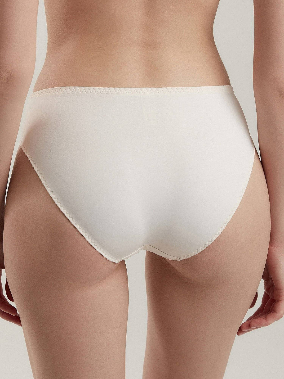 Off-white bikini-style panties with a visible zig-zag stitch pattern along the leg and waist edges shown from behind on a person.