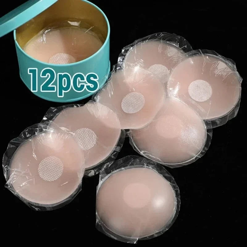Twelve circular, beige silicone nipple covers are displayed with several individually wrapped in plastic packaging next to a round teal storage tin.
