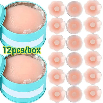 Twelve reusable silicone nipple covers are displayed next to two light blue circular storage tins, showing both flower-shaped and round designs in a soft beige color.