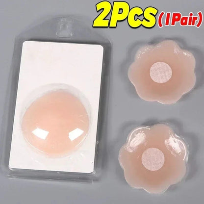 Two adhesive nipple covers in a light beige tone, one packaged in a clear plastic blister pack and two loose flower-shaped covers resting on a flat grey surface.
