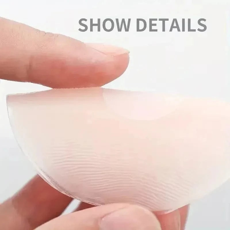 A beige, translucent, crescent-shaped silicone breast pad is being held between a person's thumb and index finger.