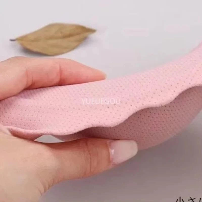 A hand holds a soft, light pink, curved foam pad with a textured, dotted surface against a plain light background.