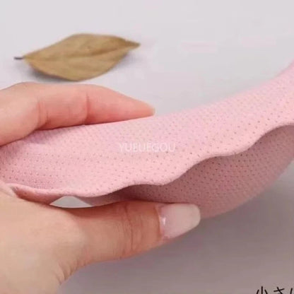 A hand holds a soft, light pink, curved foam pad with a textured, dotted surface against a plain light background.