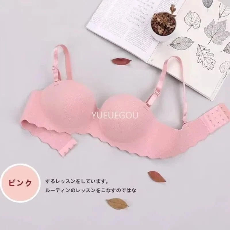 A pink, seamless wireless bra with a scalloped edge lies on a light surface next to an open book and some scattered leaves.