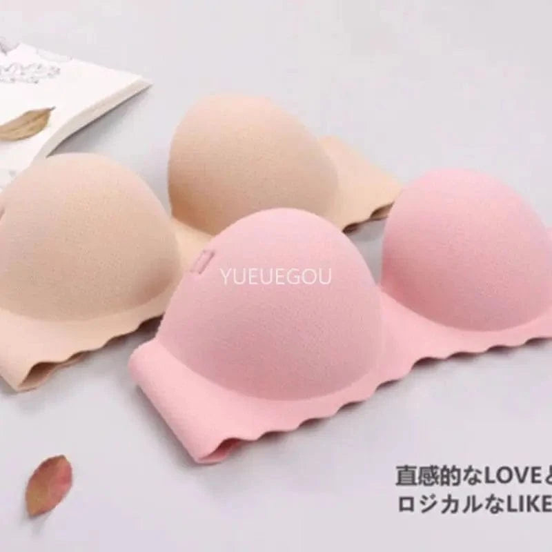Two strapless, molded cup bras in beige and soft pink rest on a surface next to a book and a dried leaf.