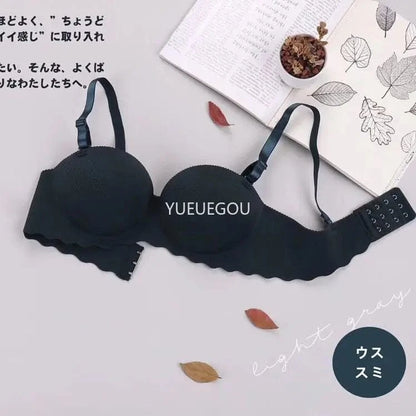 A dark-colored wireless bra with textured, molded cups and thin adjustable straps lies flat on a light gray surface next to an open book and decorative leaves.