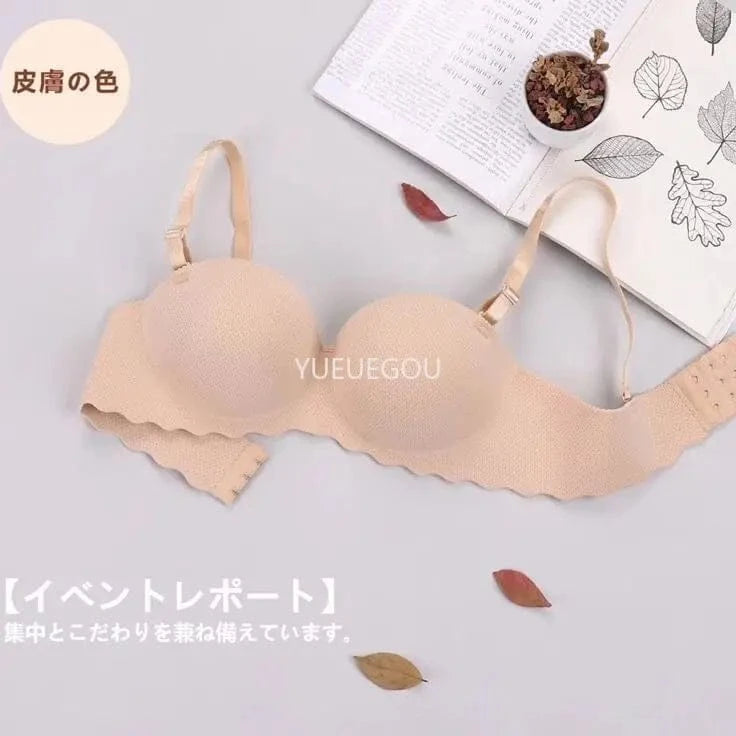 A beige strapless bra with scalloped edges is laid flat on a light grey surface next to an open book and dried leaves.