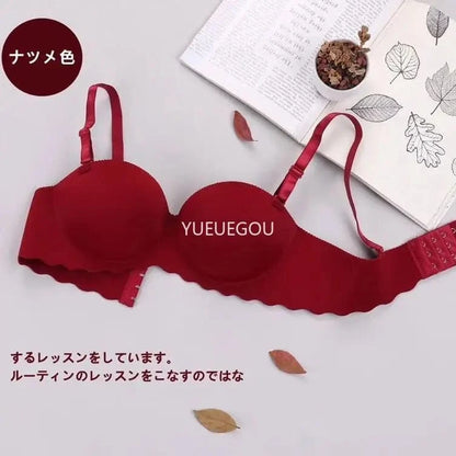 A maroon strapless bra with a textured fabric finish and scalloped edges is displayed on a flat surface next to an open book and a small bowl of dried flower petals.