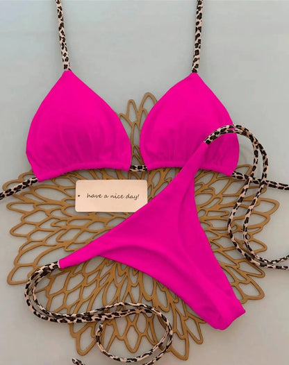 A hot pink bikini set featuring triangle cups and matching bottoms with leopard print straps, laid out on a gold decorative mat.
