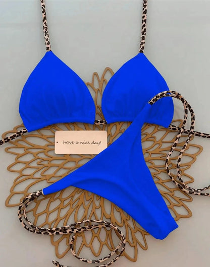 A bright blue bikini set with leopard print straps laid out on a gold decorative placemat with a small note that says have a nice day.