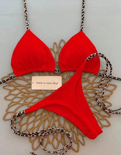 A red bikini set with thin leopard print straps laid out on a gold decorative placemat next to a small note that says have a nice day.