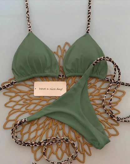 A sage green triangle bikini set with leopard print straps and matching side-tie bottoms laid out on a gold decorative placemat.