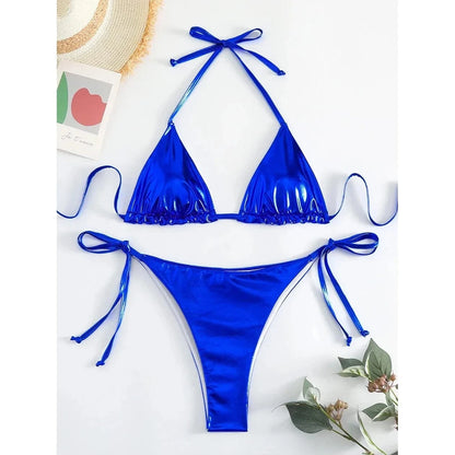 A metallic cobalt blue bikini set with a triangle top and high-cut tie-side bottoms, displayed on a flat surface with decorative elements.