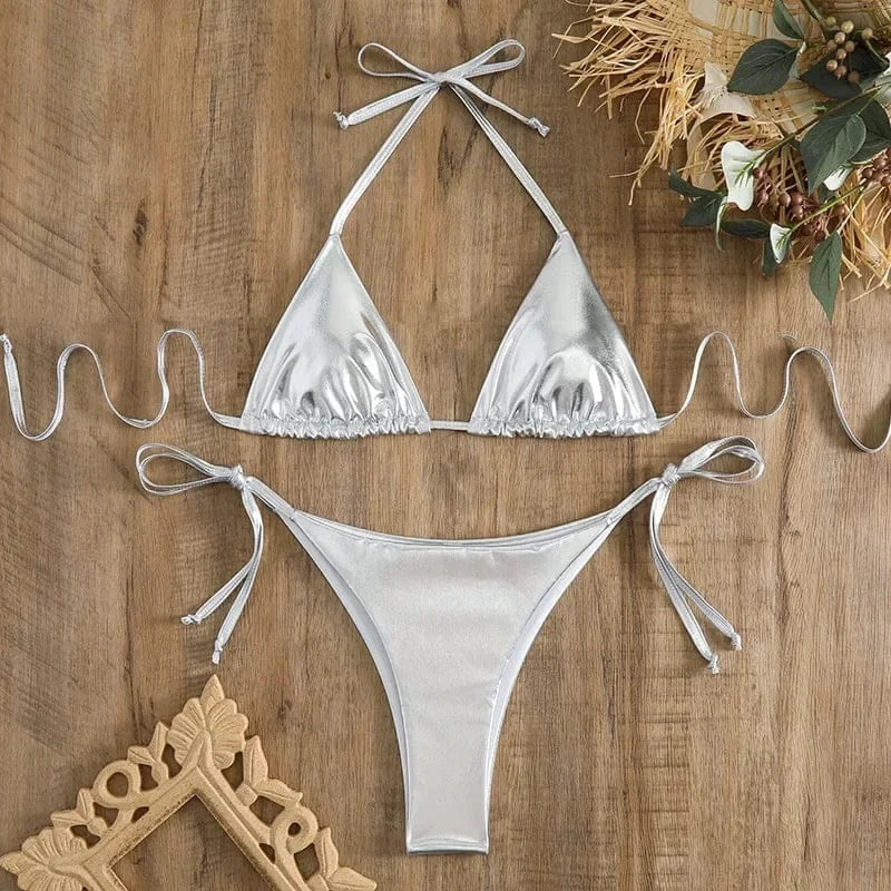 A metallic silver two-piece string bikini set featuring triangular cups and side-tie bottoms laid flat on a wooden surface.