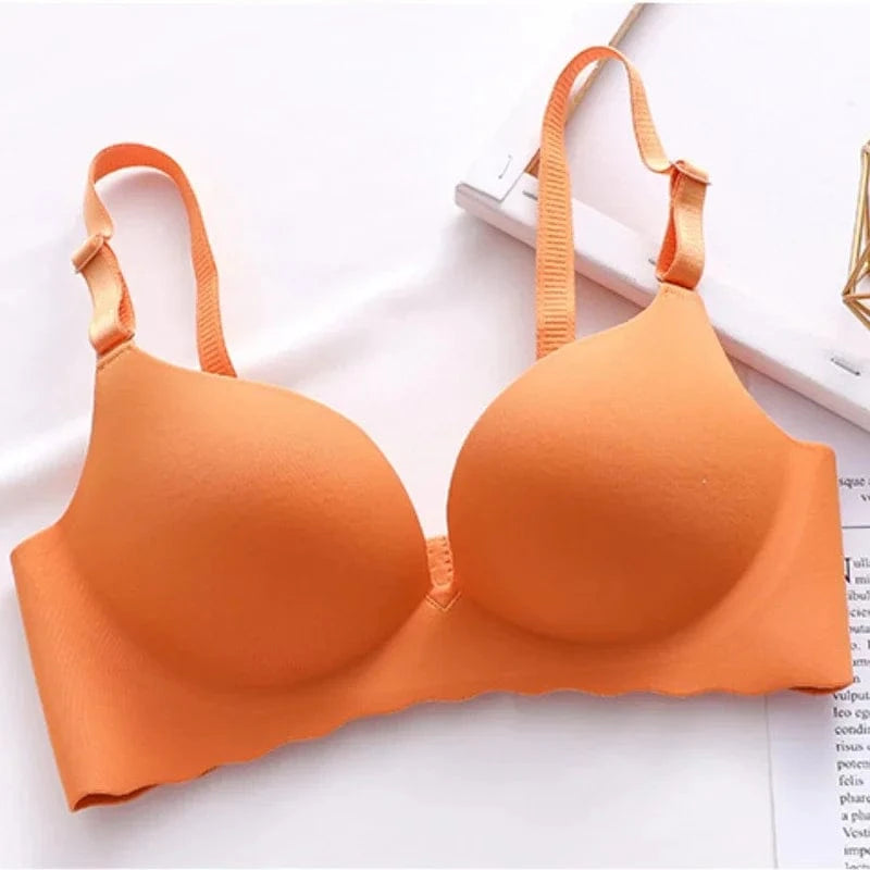 An orange seamless bra with adjustable straps sits on a white surface next to a white frame.