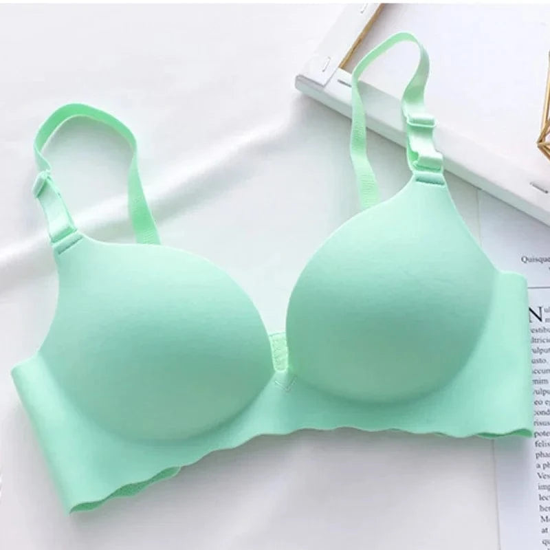 A mint green seamless wireless bra with molded cups and adjustable shoulder straps rests on a white surface next to a document.