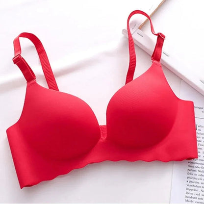 A seamless, wire-free red bra with adjustable thin straps lies flat against a white surface next to a document.