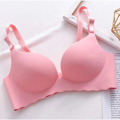 A light pink seamless bra with adjustable thin straps and molded cups, displayed against a white background with a geometric gold wire decor piece.