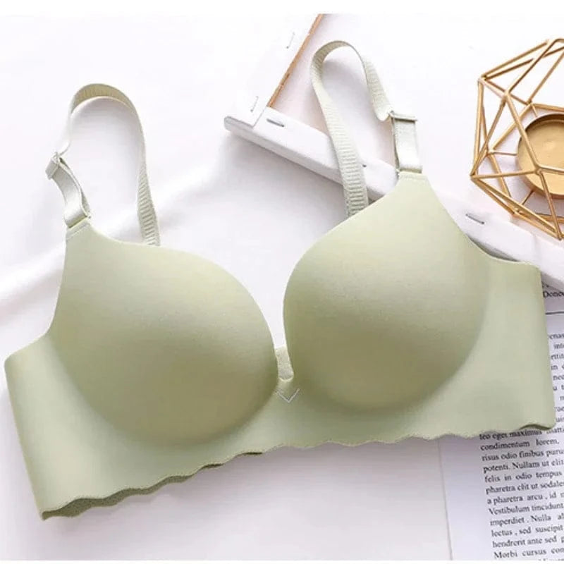 A sage green seamless push-up bra with adjustable straps and a scalloped bottom edge rests on a white surface next to a gold geometric candle holder and a piece of paper.