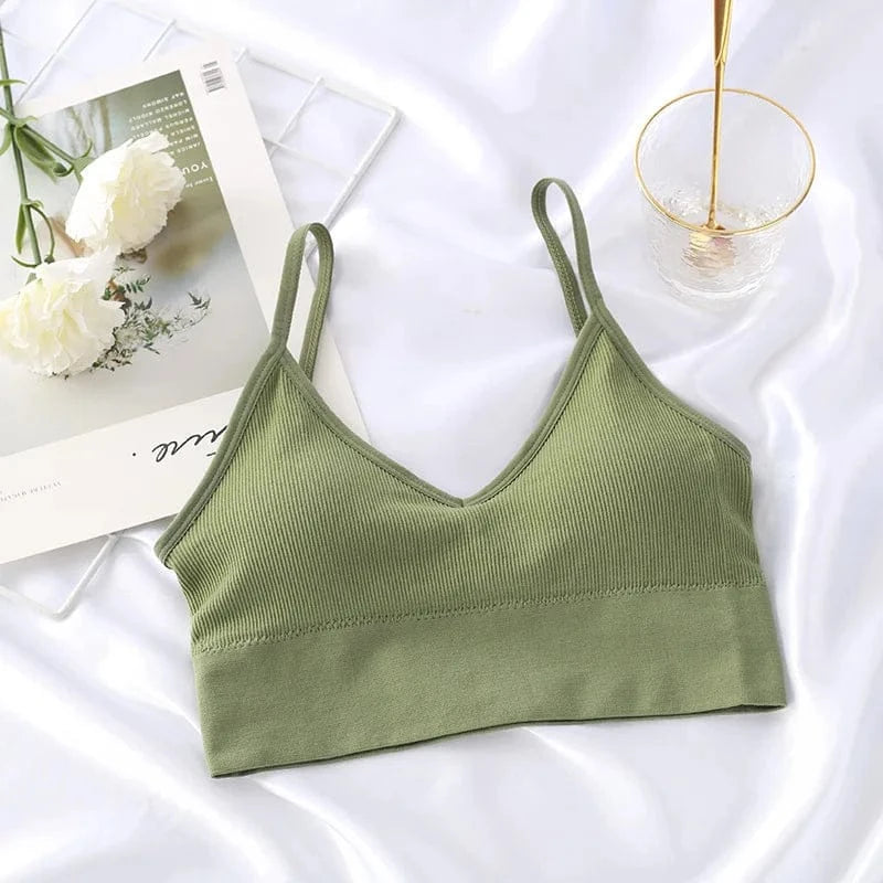 A sage green ribbed V-neck bralette with spaghetti straps laid out on a white fabric surface next to a glass of water and a floral print card.