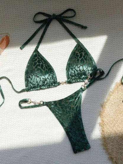 A dark green velvet bikini set with a tonal leopard print pattern, featuring triangle cups and matching thong-style bottoms accented with gold-toned hardware and faux pearls.
