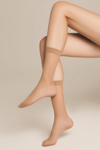A pair of sheer beige ankle-high stockings worn on legs posed in a cross-legged seated position against a neutral background.