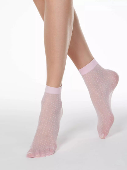 Sheer light pink ankle socks with a subtle white polka dot pattern worn on a person's feet against a plain white background.