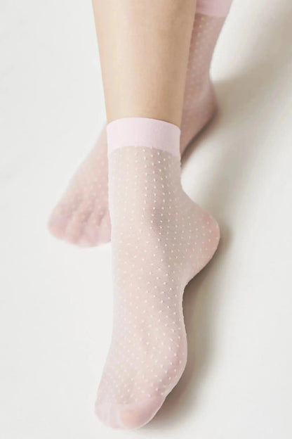 Sheer light pink ankle socks with a small white polka dot pattern and a solid pink cuff worn on a person's feet.