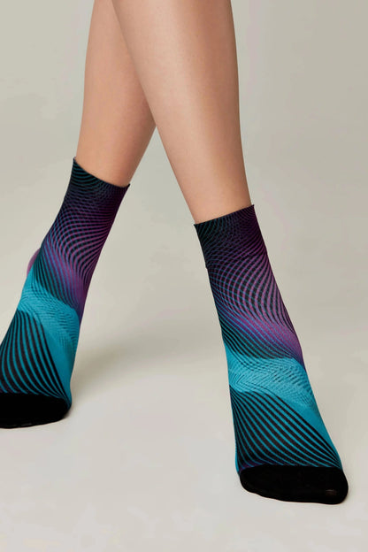 Ankle socks featuring a vibrant gradient pattern of purple and teal with black wavy linear details and solid black toe sections worn on a person's legs.