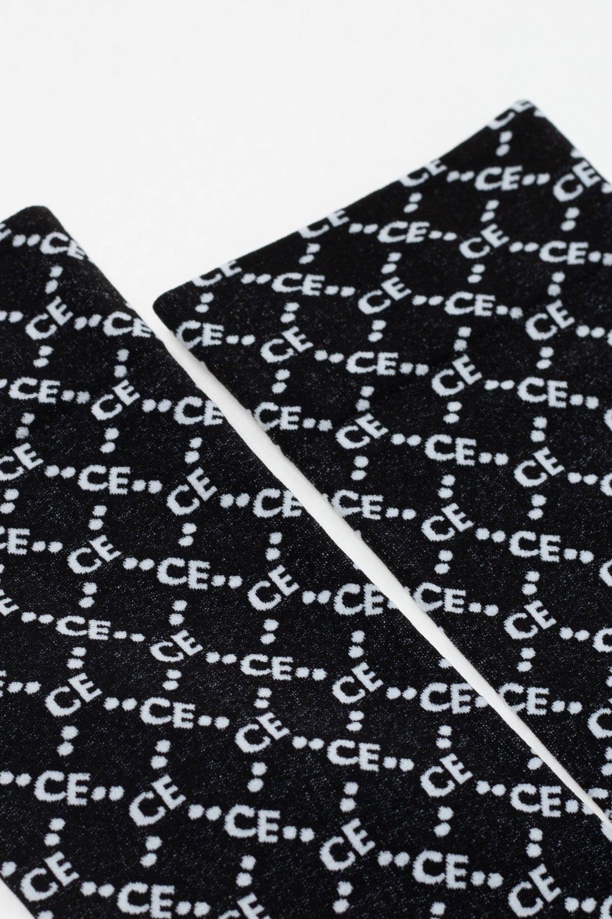 Two black fabric panels with a repeating white logo pattern featuring the letters CE separated by dots are displayed against a plain white background.